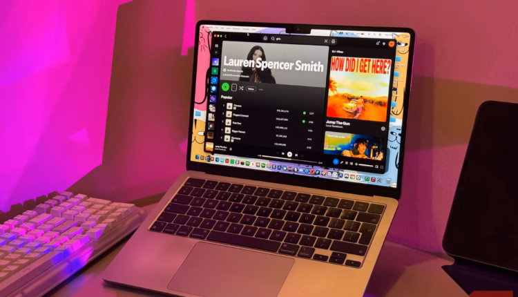 Macbook laptop displaying music streaming interface with colorful neon pink and orange lighting setu.avif