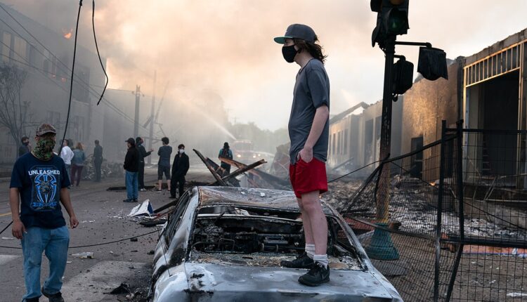 1280px A man stands on a burned out car on Thursday morning as fires burn behind him in the Lake St.jpeg