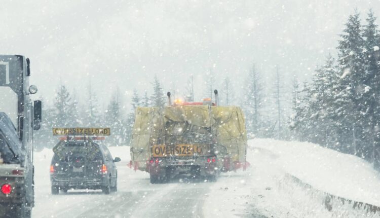 Slow moving oversize load being transported by a semi truck over a slippery winter interstate freewa.jpeg